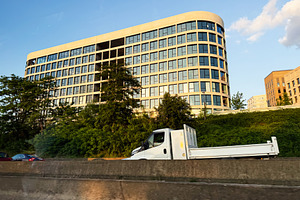 Modern office building with glass facade and delivery truck on highway in Paris, a Photo by AS photostudio