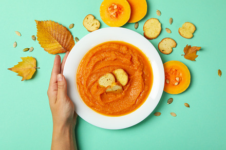 Woman hand holds plate of pumpkin soup on mint background, a Food & Drink Photo by AtlasStudio PRO