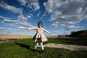 Young girl spinning and playing outdoors in a pink dress under dramatic blue sk, a Person Photo by AS photostudio