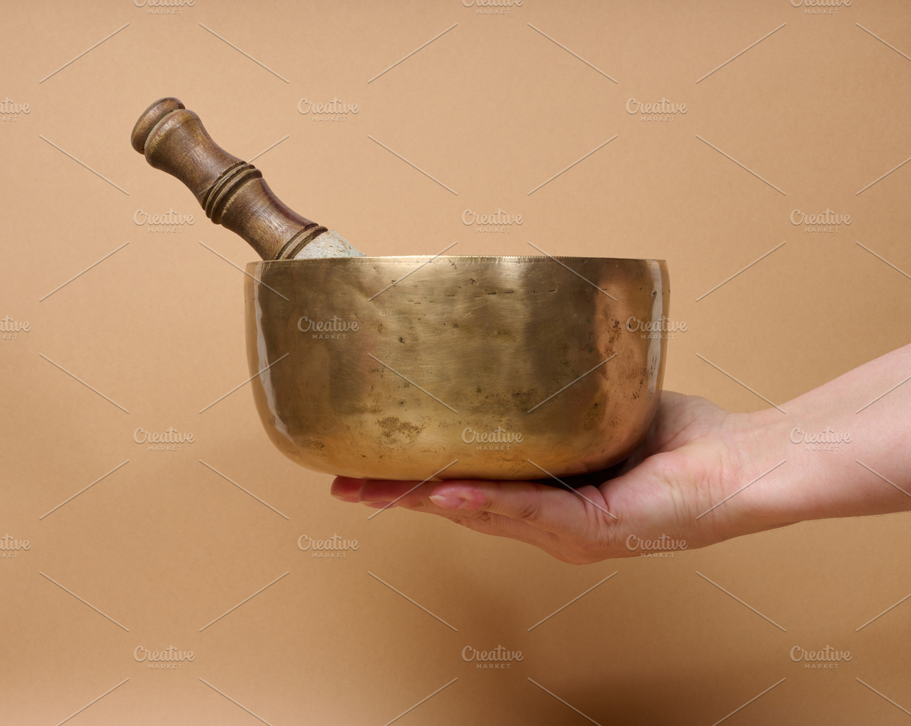 A copper singing bowl and a wooden mallet in a woman's hand, a Health & Medical Photo by ndanko