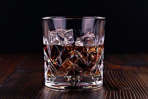 Glass of scotch whiskey and ice on wooden table, a Food & Drink Photo by AlyaAnd