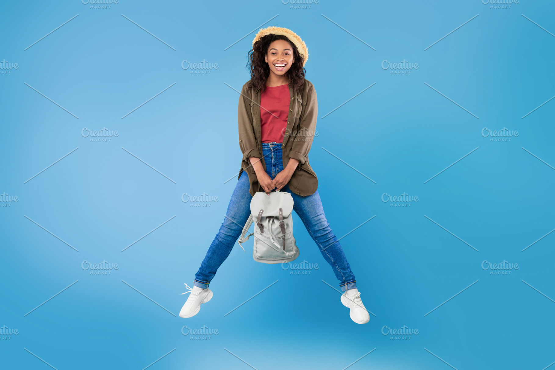 Full length portrait of positive young black woman with backpack jumping on blu, a Photo by Prostock-Studio