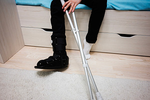 Close-up of a leg in a medical orthopedic boot with crutches indoors, a Health & Medical Photo by AS photostudio