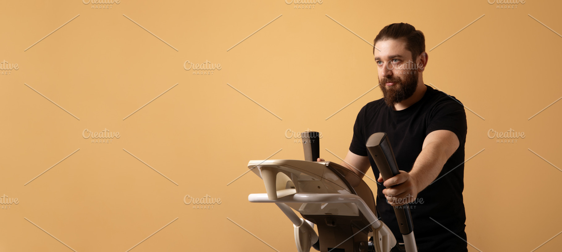 Bearded man in black t-shirt using elliptical machine against pl, a Person Photo by Ales Munt