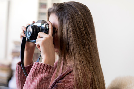 Young woman taking a photo with a vintage camera indoors., a Photo by RF Images