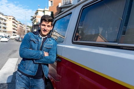 A Happy young man leaning at the retro mini van