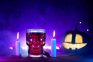 Halloween party concept. A glass of bloody red beer, burning candles and a glow
