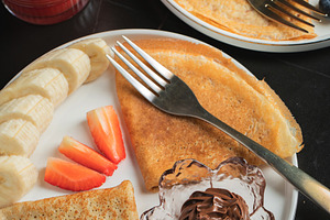 A plate of crepes filled with chocolate spread and topped with banana slices an, a Food & Drink Photo by Budarinphoto