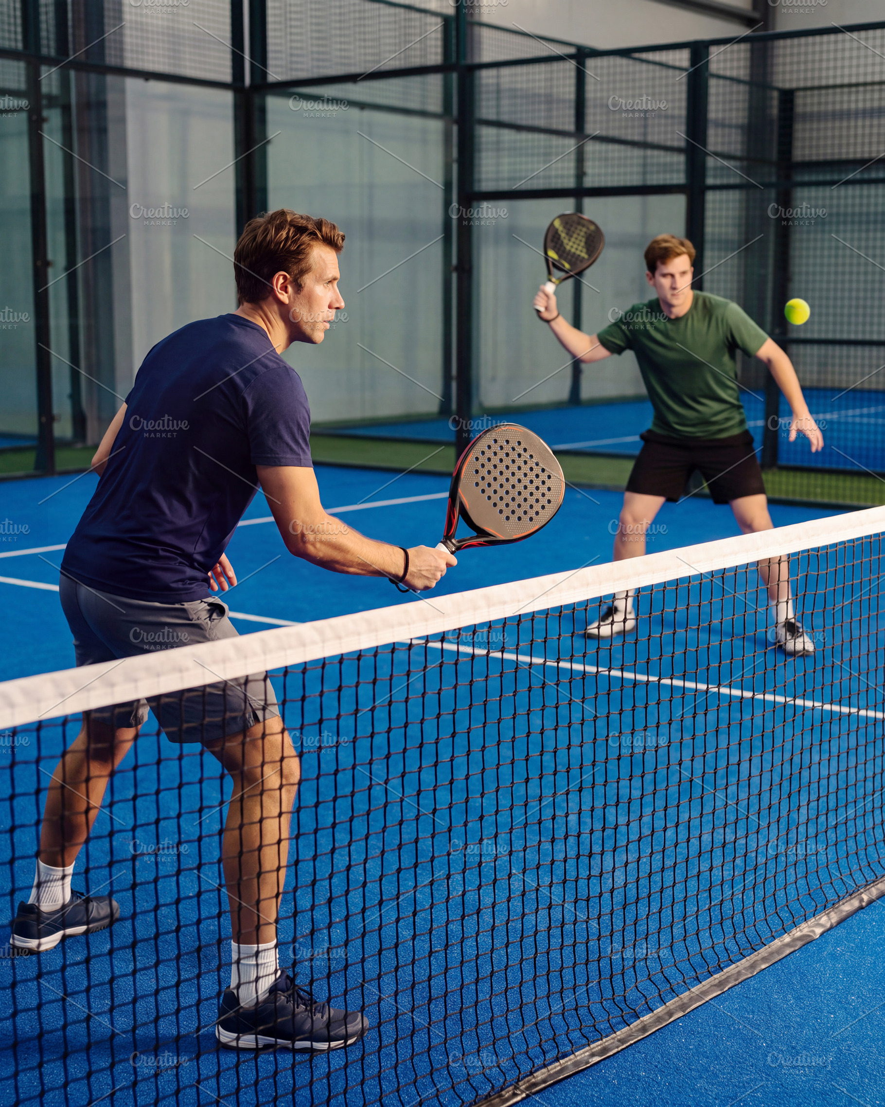 Men playing dynamic padel match on blue court with glass walls i, a Sports & Recreation Photo by Volff