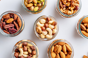 Assorted nuts in glass jars on white surface, a Food & Drink Photo by AlyaAnd