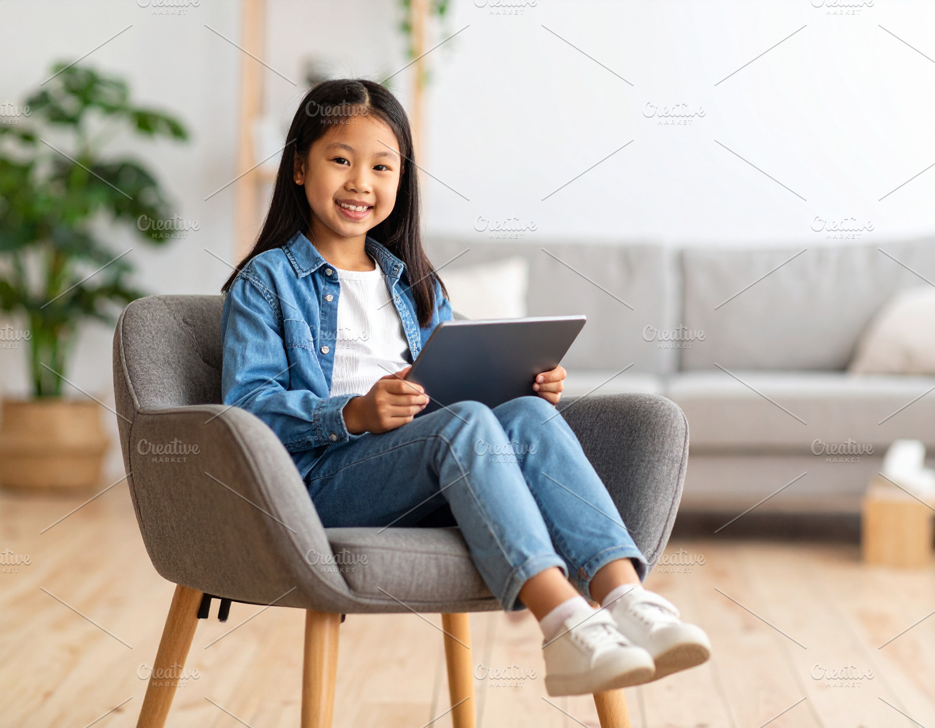 Girl with a tablet sitting on chair at living room while smiling, a Person Photo by DanFLCreativo