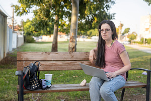 Woman sitting on a wooden bench in a park with a laptop, looking, a Person Photo by Imaginarium