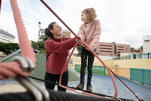 Mother helping her daughter balance on playground climbing ropes, a Person Photo by etorres69