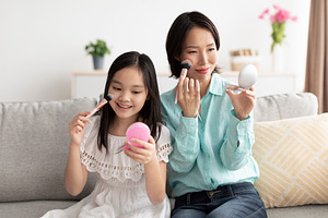 Happy mature Asian woman with her cute little granddaughter applying makeup, ha, a Photo by Prostock-Studio