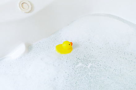 Bathtub with foam bubbles and yellow playful rubber duck in bubb