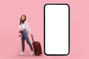 Female Tourist Near Phone Screen Posing With Suitcase, Pink Background, a Photo by Prostock-Studio