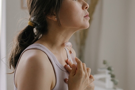 Beautiful asian woman doing neck massage with pink quartz roller during daily b, a Person Photo by Anikona