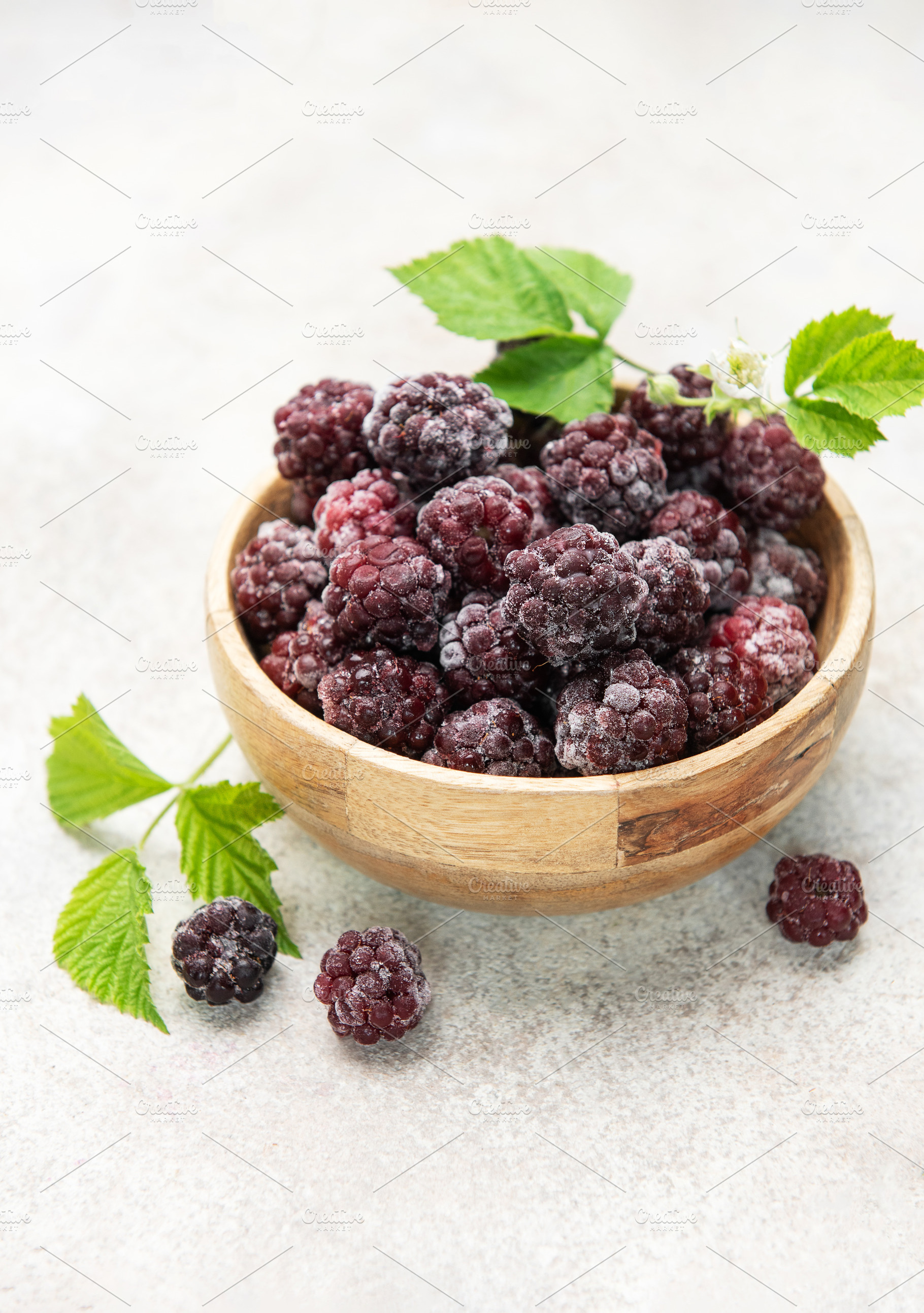 Frozen blackberries in wooden bowl with green leaves, a Food & Drink Photo by Olena Rudo