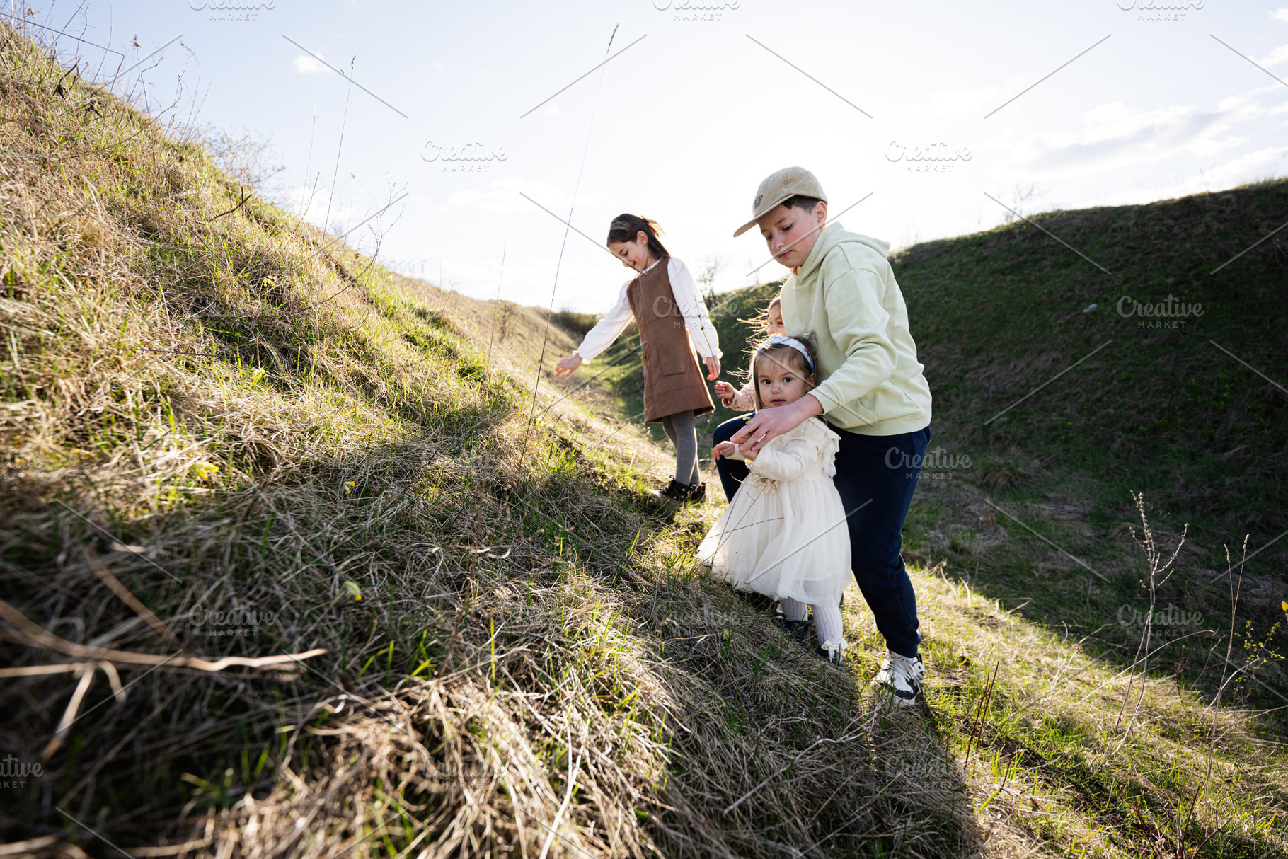 Older brother helping little sister walk up grassy hill during family outing in, a Person Photo by AS photostudio