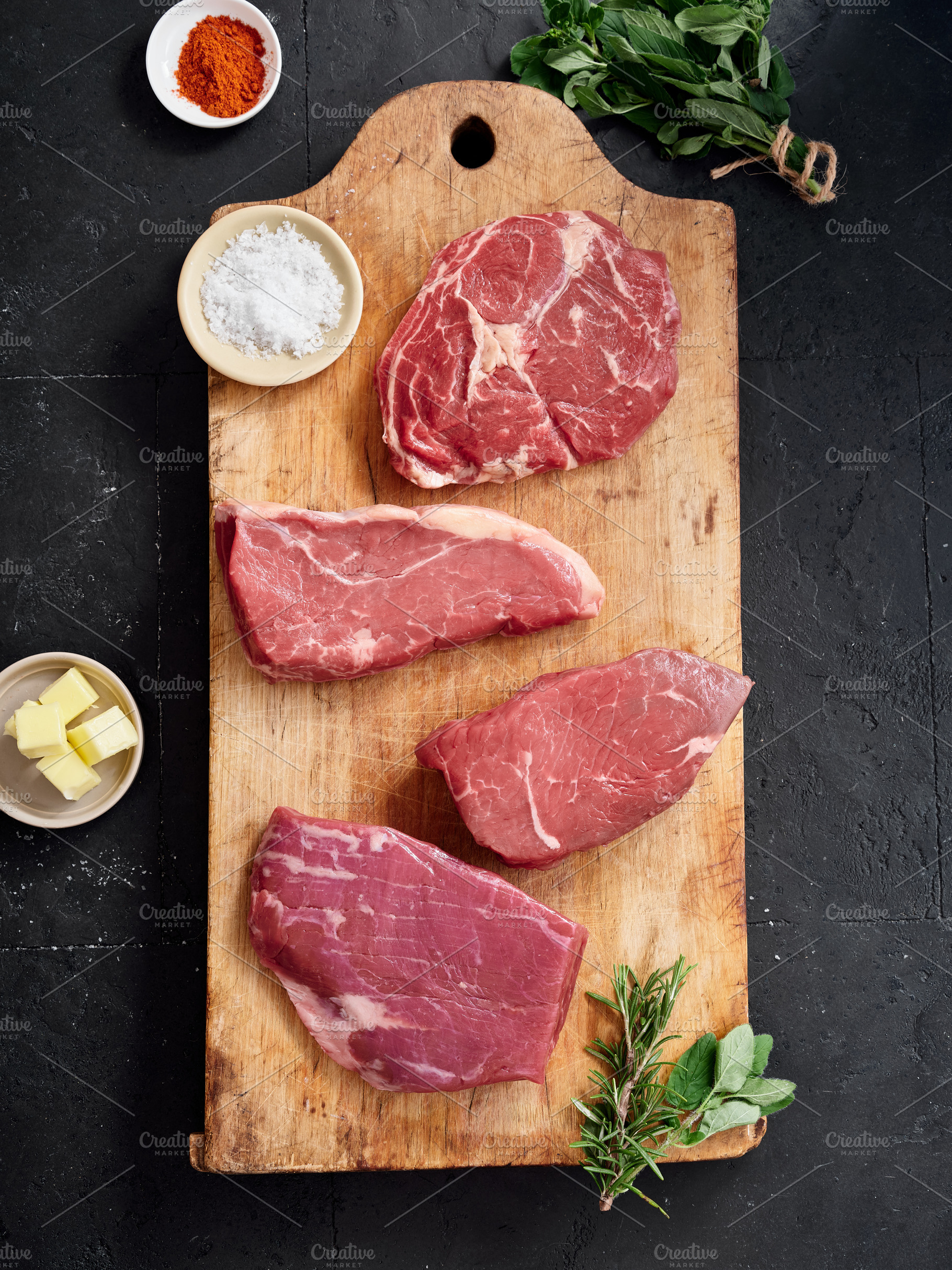 Raw rib-eye, roast beef, flank and rump steak arranged on a wooden cutting boar, a Food & Drink Photo by Asya Nurullina