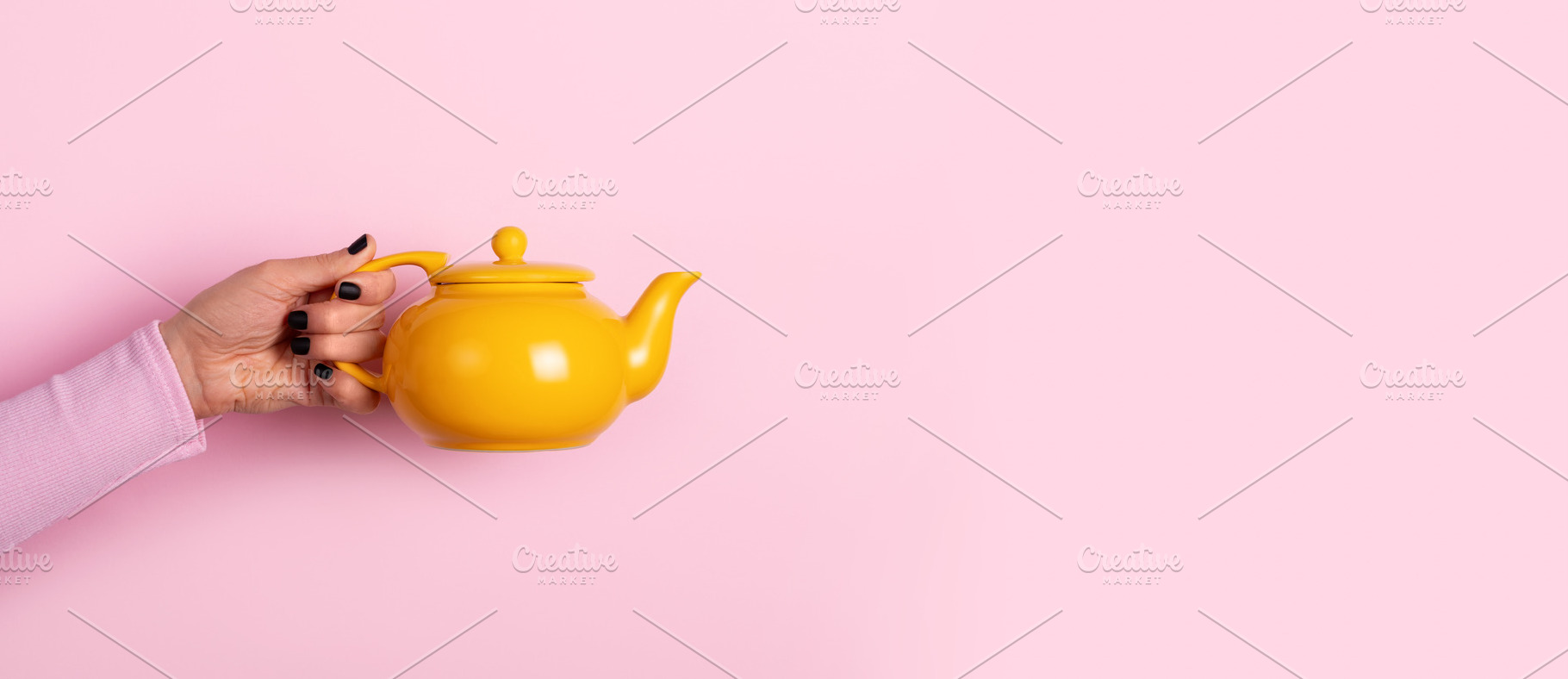 Female hand holding a bright yellow teapot against a pastel pink, a Holiday Photo by Ales Munt