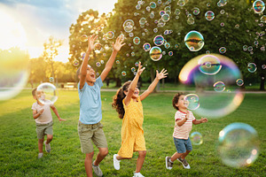 Happy children chasing and popping soap bubbles in a grassy park, a Person Photo by DanFLCreativo