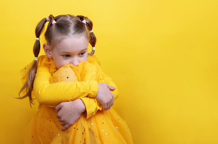 Pensive girl in yellow dress hugging her knees and looking sidew