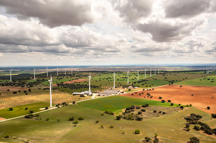 Multiple wind turbines rotating over colorful farmland under cloudy sky