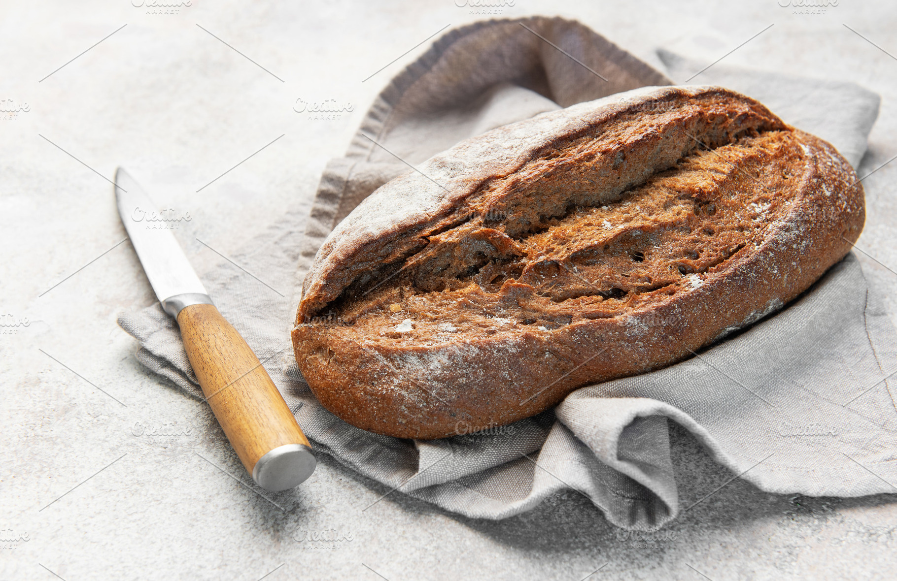 Rustic dark bread loaf with knife on napkin, a Food & Drink Photo by Olena Rudo