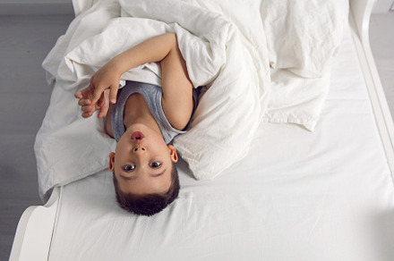 child boy is mad having fun in a white bed in the children's room with a blanke, a Person Photo by SaulichPhoto