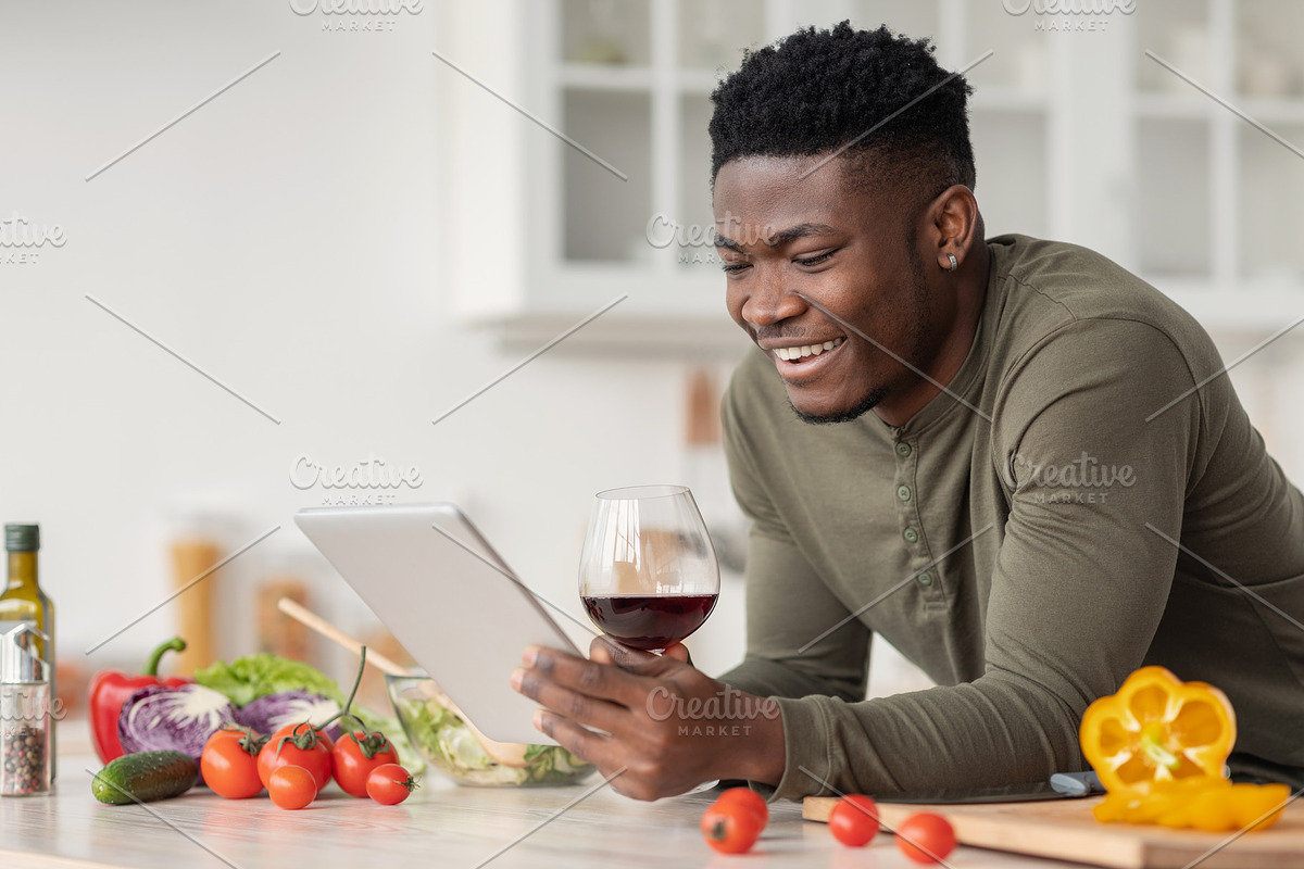 Happy Black Man Using Digital Tablet And Drinking Red Wine In Kitchen, a Photo by Prostock-Studio (Photo 2 of 2)