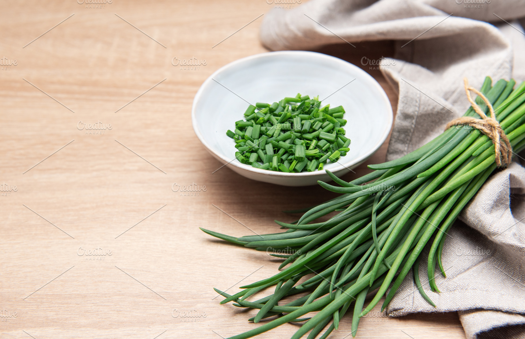 Freshly cut chives in a bowl resting on wooden table, a Photo by Olena Rudo