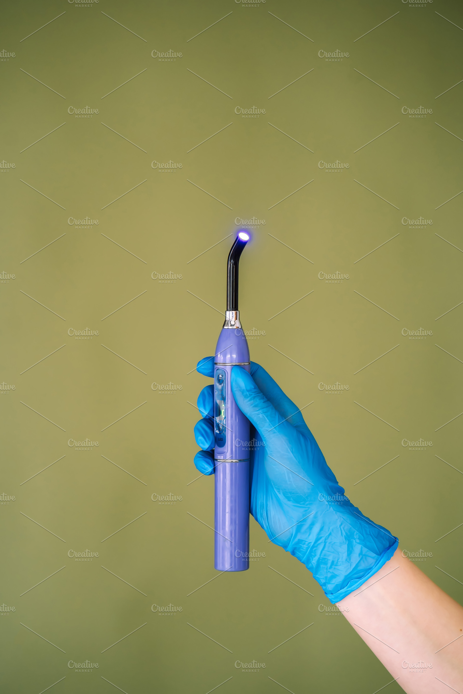 Dental curing light in gloved hand on green background, a Technology Photo by Red Hot Chili Pepper Shop