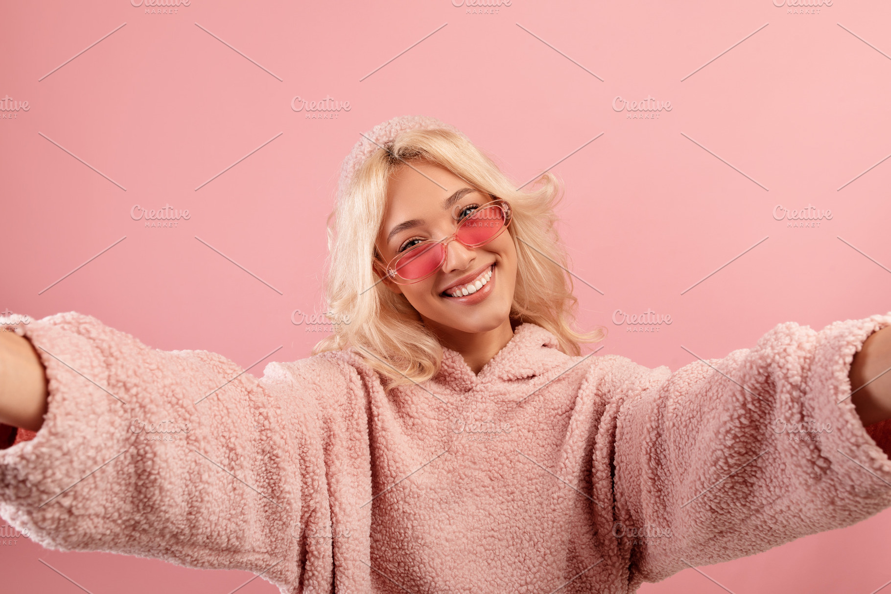 Happy blogger lady making selfie, wearing colorful glasses and hoodie, posing a, a Photo by Prostock-Studio