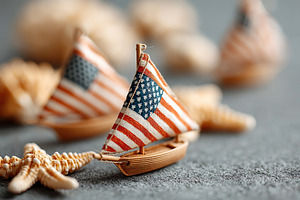 Miniature sailboats with American flags on a textured surface near seashells, a Holiday Photo by AlyaAnd