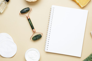 Flat lay of skincare essentials with notebook mockup including marble face roll, a Photo by matucha