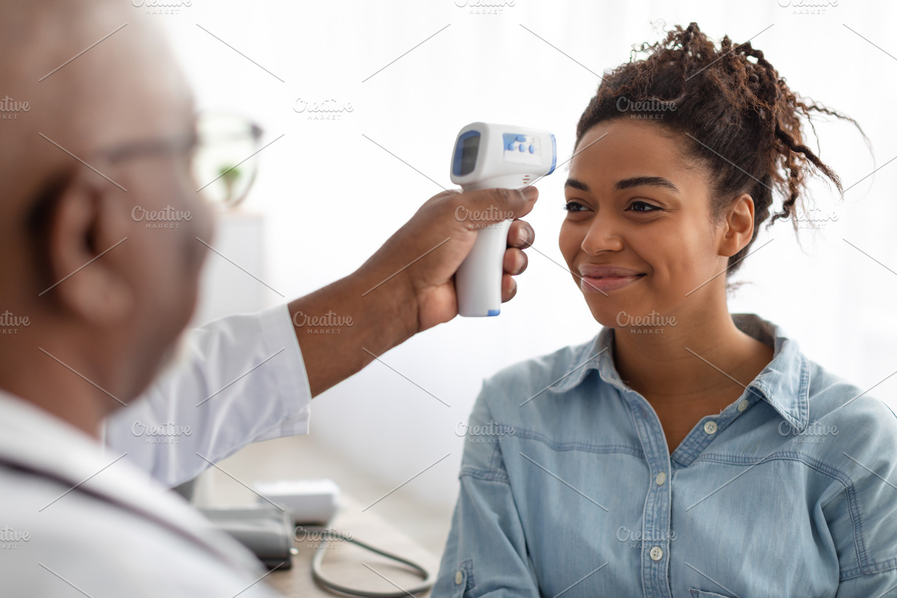 Doctor checking temperature of young black woman using infrared thermometer, a Photo by Prostock-Studio