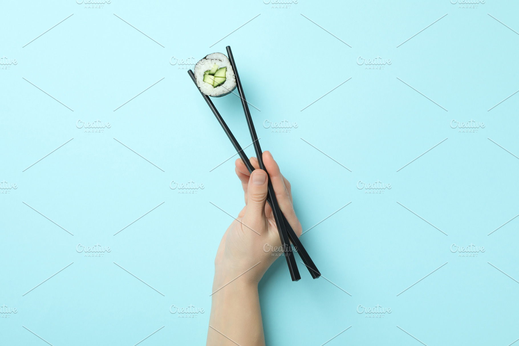 Female hand holding maki with chopsticks on blue background, a Food & Drink Photo by AtlasStudio PRO