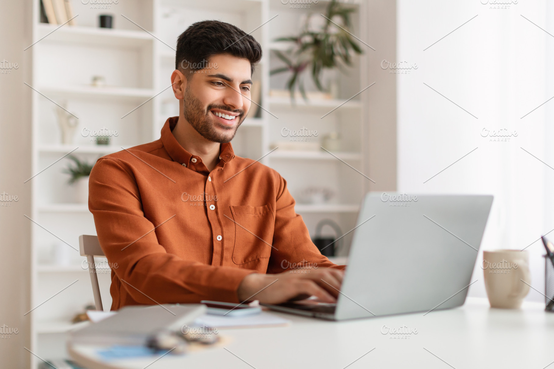 Arab man using laptop sitting at desk in office, a Photo by Prostock-Studio