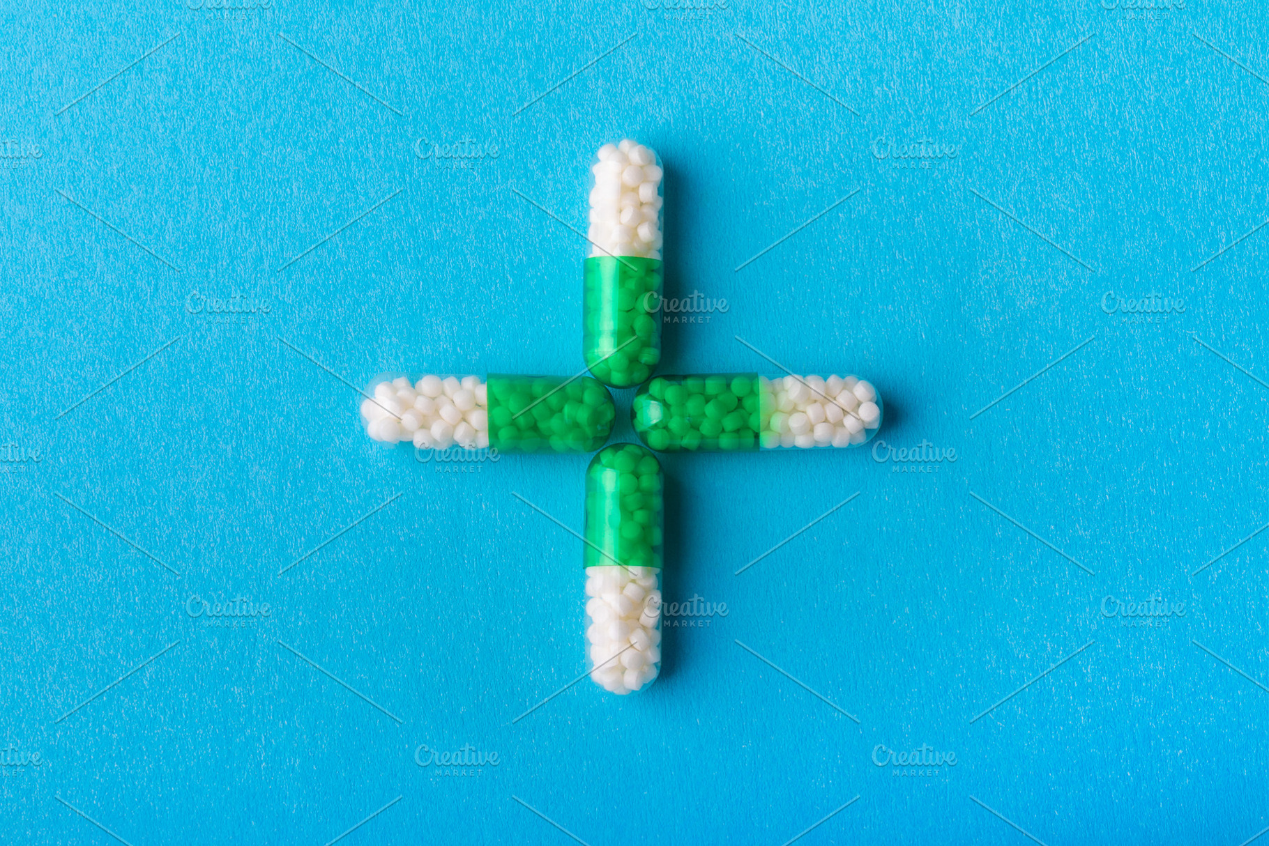Four green and white capsules arranged in a plus sign on a vibrant blue backgro, a Health & Medical Photo by Ales Munt