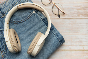 Wireless headphones lying on folded jeans and eyeglasses on wood, a Business Photo by Olena Rudo
