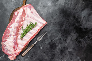 Pork spareribs raw whole rack with rosemary on cutting board ove