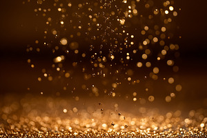 Golden glitter particles falling and shimmering on a textured surface, creating, a Photo by Studio ANNA