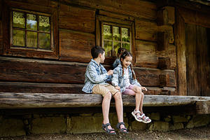 Two children sitting on a wooden bench outside a rustic cabin, a Person Photo by AS photostudio