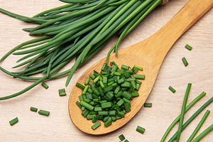 Freshly cut chives resting on wooden spoon and table, a Food & Drink Photo by Olena Rudo