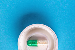 Green and white capsule pill placed inside a white bottle cap on a vibrant blue, a Health & Medical Photo by Ales Munt