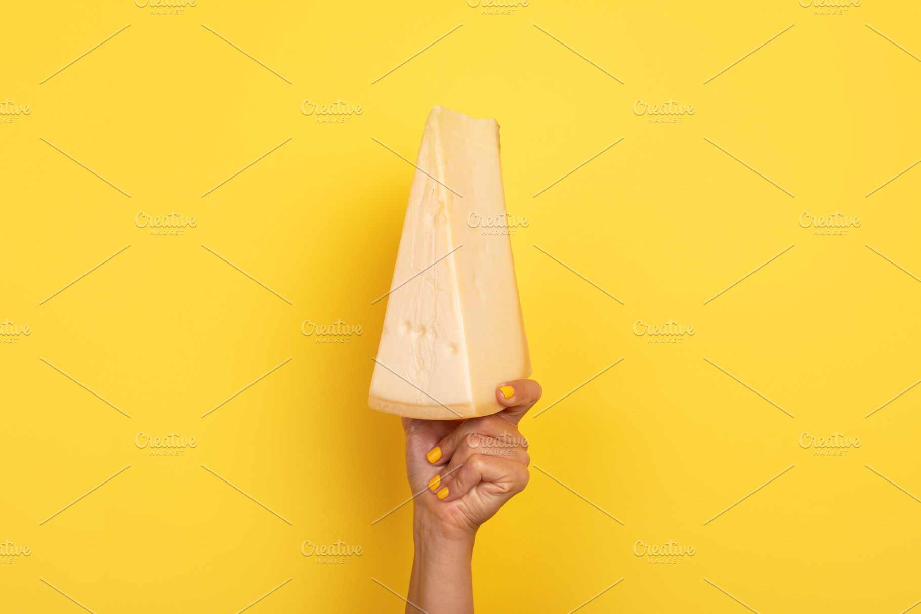 Hand with yellow nails holding a large wedge of cheese raised a, a Food & Drink Photo by Ales Munt