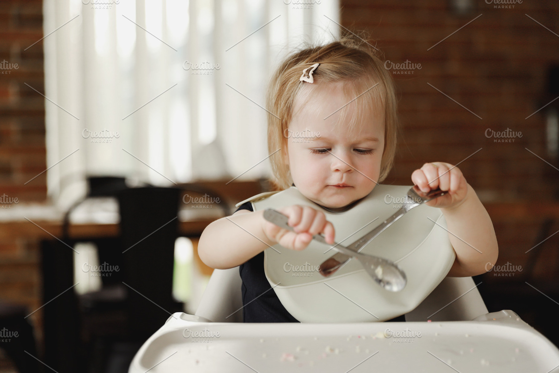 Infant girl or toddler sitting on high chair. Eating food by herself using spoo, a Person Photo by Lenor4ik