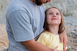 Loving father hugging his smiling daughter outside on a rocky beach, showing fa, a Person Photo by Ales Munt