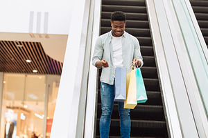Happy black man holding shopping bags looking inside, a Photo by Prostock-Studio
